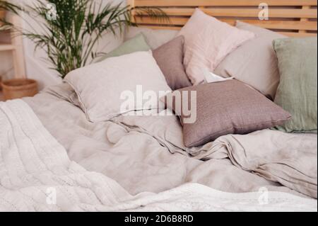 very cozy soft pastel place to relax and sleep. Pillows in soft maroon and green, rumpled knitted beige blanket on large bed. Selective focus Stock Photo