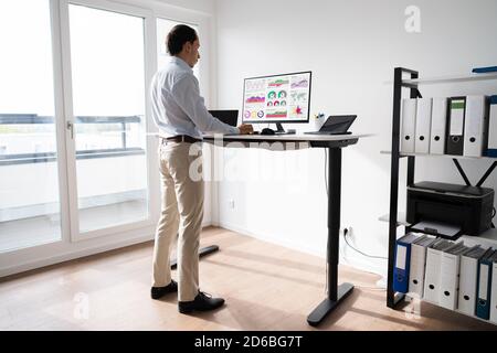 Man Working On Computer At Standing Desk In Home Office Stock Photo