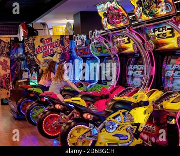 Mackay, Queensland, Australia - February 2020: Two young girls riding a motor cycle simulator in an amusement arcade Stock Photo