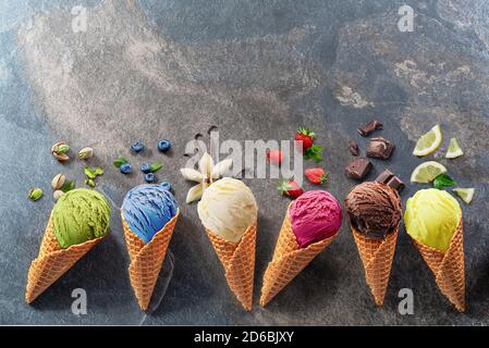 Set of various colorful ice creams in waffle cones with fruits slices on the grey background. Lay out view. Stock Photo