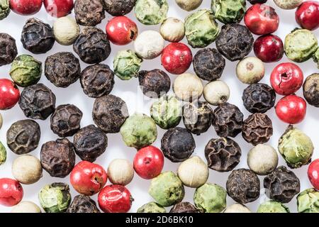 Black, white, green and red peppercorns isolated on white background. Stock Photo