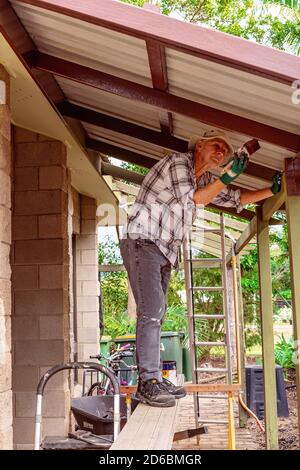 Townsville, Queensland, Australia - June 2020: Man standing on trestles painting roof rafters of residential house Stock Photo