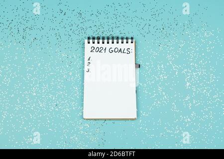 Small notebook on blue confetti background with written 2021 goals for new year. Resolutions list Stock Photo