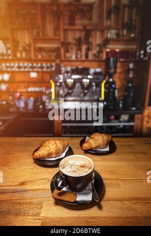 Coffee drink served with croissant on wooden table with blur cafeteria as background Stock Photo