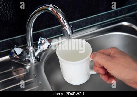 clean filtered water flows from the tap. Danger of untreated drinking water. filling water in white porcelain glass at kitchen sink Stock Photo