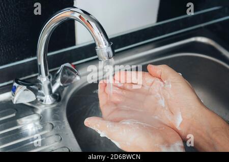 a young guy washes his hands with soap under the faucet against the background of a metal sink. Virus prevention. Hygienic procedure. Wash your hands. Stock Photo