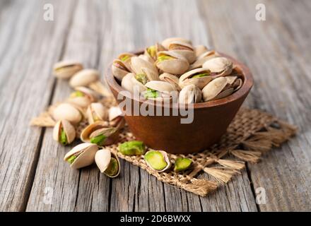 Close up of pistachios in a bowl set against an old wooden backdrop Stock Photo