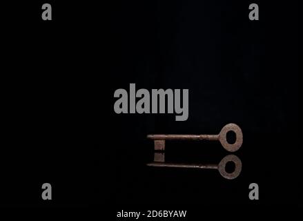 antique rusted chest key in dark black background with reflection on floor Stock Photo