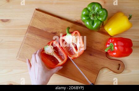 Top View of Hand Cutting Red Bell Pepper on a Wooden Cutting Board with Three-color Bell Peppers Scattered Around Stock Photo