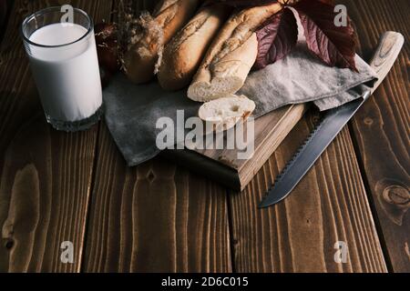 Close up fresh french baguette with glass of milk on a wooden table. Tomato and knife Stock Photo