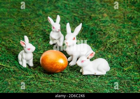 Happy Easter. Congratulatory easter background. Little white bunnies around golden egg on a background of moss. Stock Photo