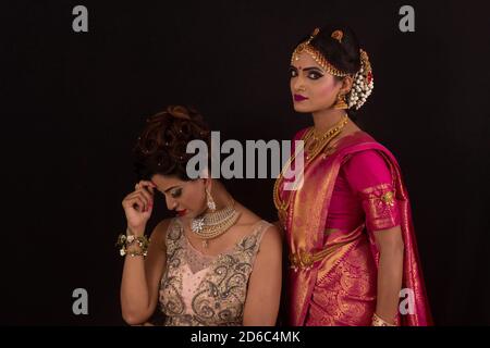 Indian model in pink and golden dress and Young South Indian model in bridal red sari with golden jewelry set Stock Photo