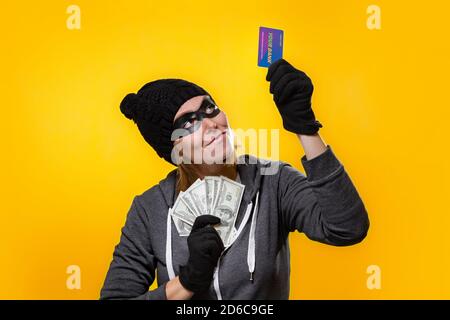 The concept of online fraud and shopping in online stores. A woman wearing black glasses, a mask and a black hat, holding a wad of dollars and a Bank Stock Photo