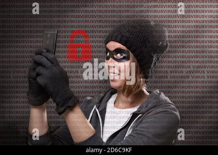 The concept of cybercrime and hacking, the dark Internet. Portrait of a woman in a black hat, gloves and mask, who holds a mobile phone and smiles Stock Photo