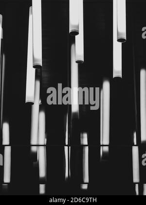 Several glowing cylindrical lamps in the dark. The cylinders are reflected in a glossy mirror surface. Abstract black and white image. Stock Photo
