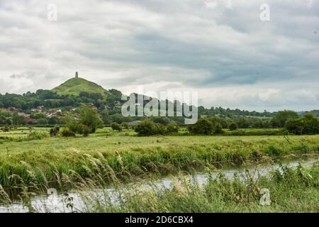 Glastonbury Tor in the distance towering over Glastonbury township. A small local stream cuts across the foreground. No people. Copy space. Stock Photo