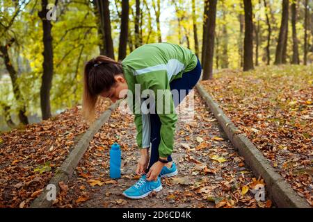 Runner tying shoe laces in autumn park. Woman training with water bottle. Active healthy sportive lifestyle Stock Photo