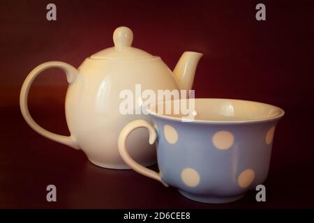 Porcelain kettle with tea cup, maroon background Stock Photo