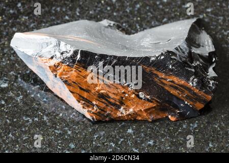 macro photography of sample of natural mineral from geological collection - unpolished mahogany Obsidian (volcanic glass) from Armenia on black granit Stock Photo