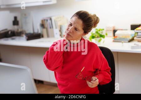 Woman massaging her neck at desk Stock Photo