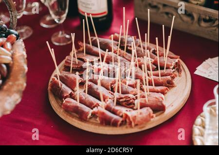 Side view of a round wooden plate with sliced and twisted pieces of meat on skewers. Catering. Stock Photo