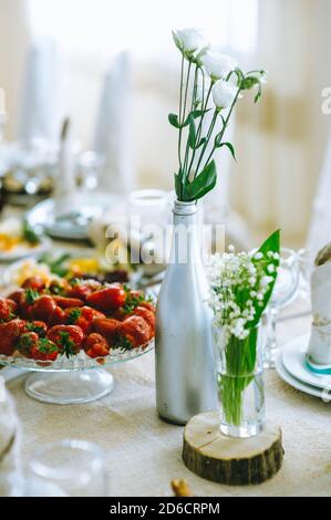 Close up of white eustoma and lily of the valley in glass vases on festive table. Stock Photo