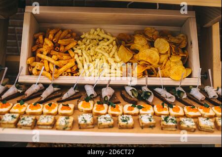 Different types of chips in a wooden box and a variety of canapes on the buffet table. Stock Photo
