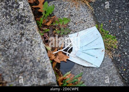 A dirty worn disposable face mask lying in a street beside a curb stone. Seen in Germany in October during corona crisis. Stock Photo