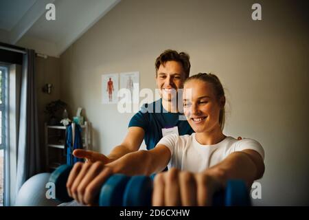 Male physiotherapist observing female patient holing weights  Stock Photo