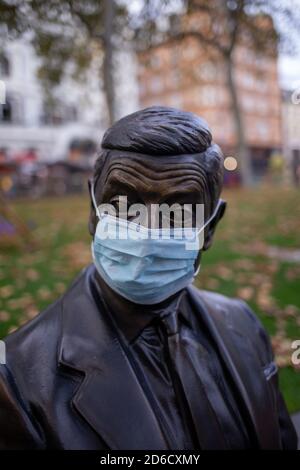 A bronze statue depicting a scene from a Mr Bean film featuring Rowan Atkinson wearing a protective mask during the COVID-19 pandemic sitting on a par Stock Photo