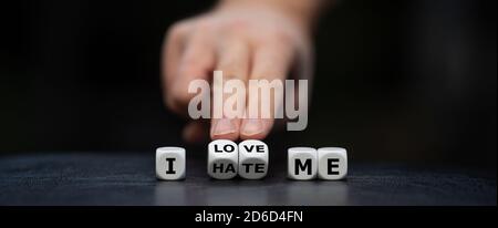 Hand turns dice and changes the expression 'I hate me' to 'I love me'. Stock Photo