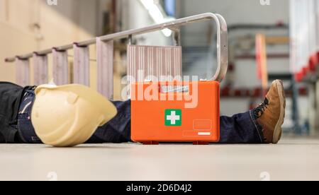 Male body lying on the floor after a work accident. Fallen ladder,    helmet and first aid kit lying next to the body. Stock Photo