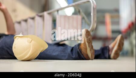 Male body lying on the floor after a work accident. Fallen ladder and safety helmet lying next to the body. Stock Photo