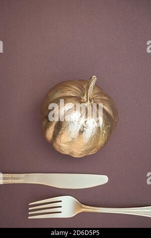 Creative Thanksgiving background. Golden colored pumpkin and cutlery on dark brown background. Flat lay, top view, copy space. Stock Photo