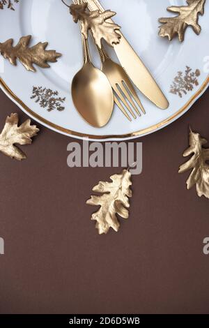 Golden colored leaves and cutlery on dark brown background. Creative autumn table setting. Flat lay, top view, copy space. Stock Photo