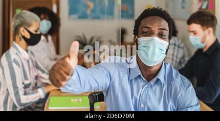 African man thumb up wearing face mask in co-working creative space with team work - Young people working during corona virus pandemic Stock Photo