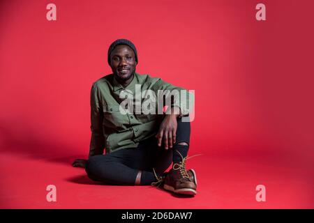 Young black man sitting relaxed on studio floor for photoshoot. Isolated. Copy space. Stock Photo