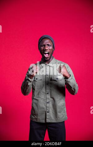 Young black man shouting with fists clenched and mouth open. Isolated. Medium shot. Stock Photo