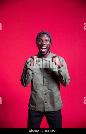 Young black man shouting with excitement with fists clenched. Isolated. Copy space. Vertical. Stock Photo