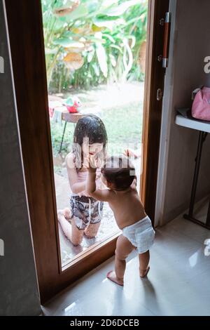 Two Asian siblings smiled at each other through the window glass while playing together at home Stock Photo