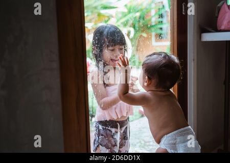 Two Asian siblings smiled at each other through the window glass while playing together at home Stock Photo