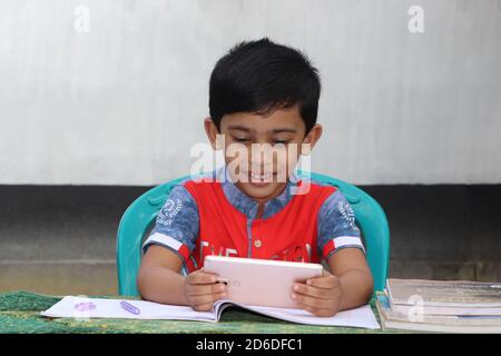 Happy little asian boy using smartphone while studying outside. Elementary school boy attending Stock Photo