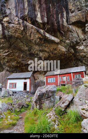 Norway landmark. Helleren old homes hidden beneath huge rock cliff in Jossingfjord. Stock Photo