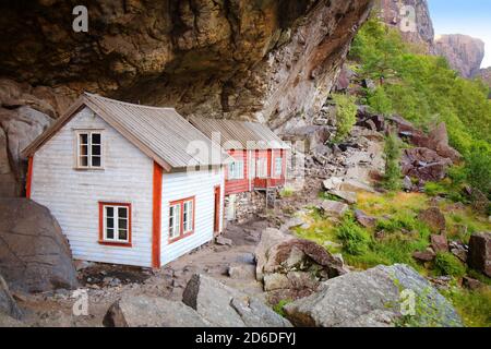 Norway landmark. Helleren old homes hidden beneath huge rock cliff in Jossingfjord. Stock Photo