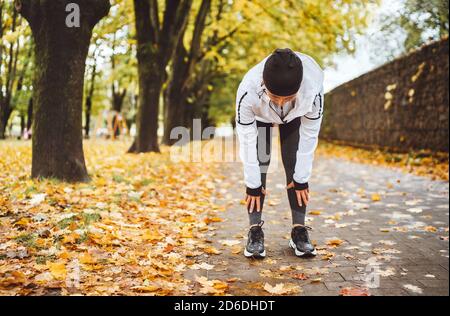 Mid aged fit athletic woman dressed modern running clothes standing and bend over to stretch the back on the footway after jogging in the autumnal cit Stock Photo