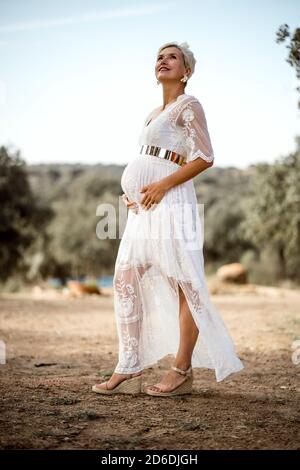 Pretty standing pregnant woman in white dress outdoor Stock Photo