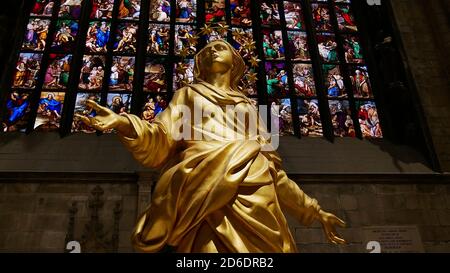 Milan, Lombardy, Italy - 11/10/2018: Golden Madonna statue in Christian Milan Cathedral (Duomo di Milano) with colorful stained glass windows. Stock Photo
