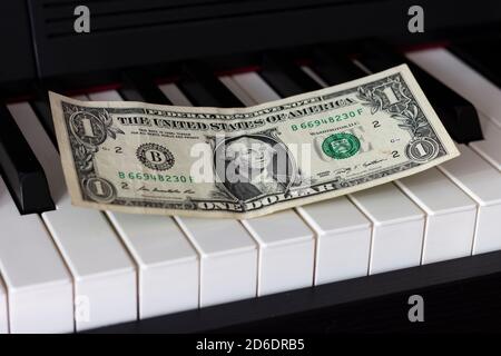 One dollar banknote lying on the piano keys. The dollar as a symbol of global economic management. Stock Photo