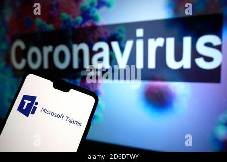 The Microsoft Teams logo seen displayed on a mobile phone with an illustrative model of the Coronavirus displayed on a monitor in the background. Stock Photo