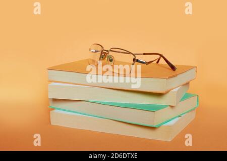 The glasses are on a stack of four books on a uniform orange background Stock Photo
